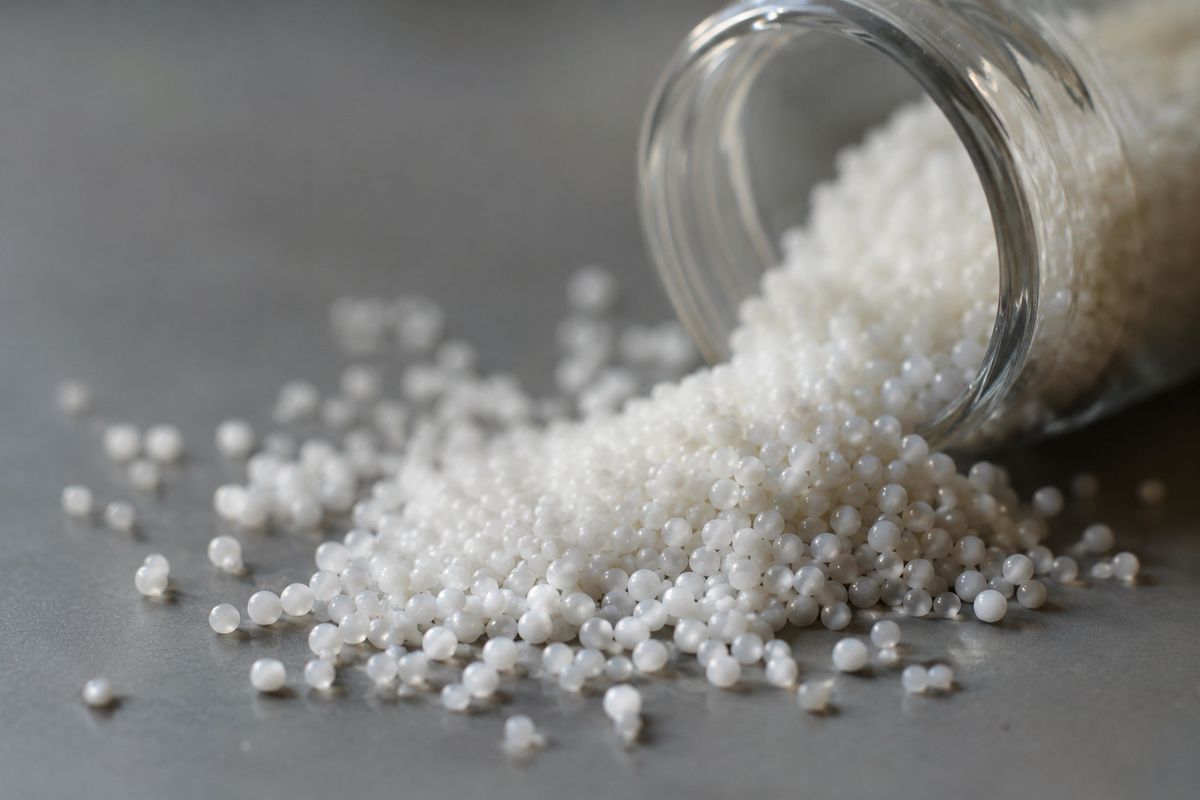 Free-flowing white silica micropearls spilling from a glass sample jar onto a laboratory surface