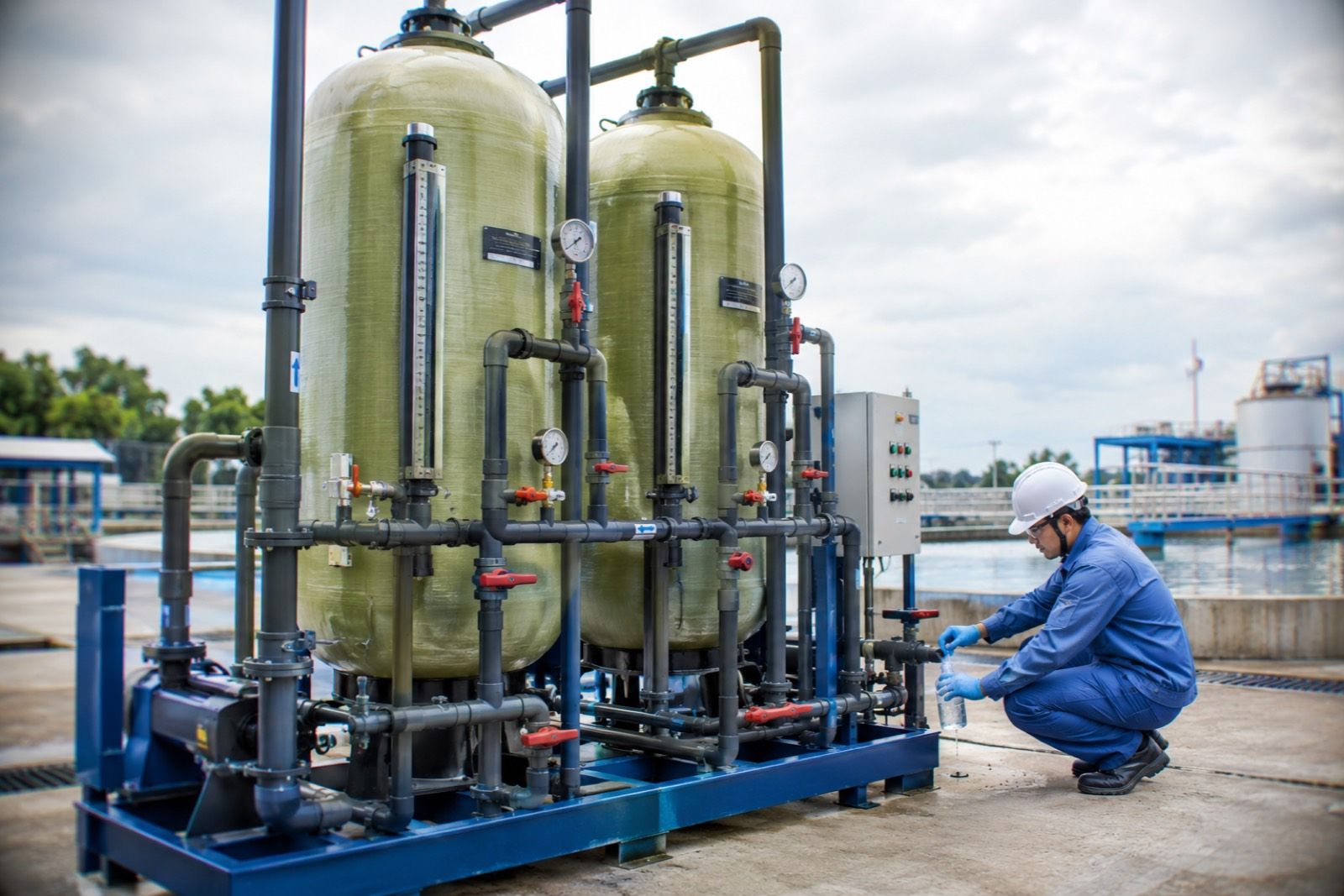 Technician taking a water sample at a fibreglass adsorption column skid in an industrial wastewater treatment plant